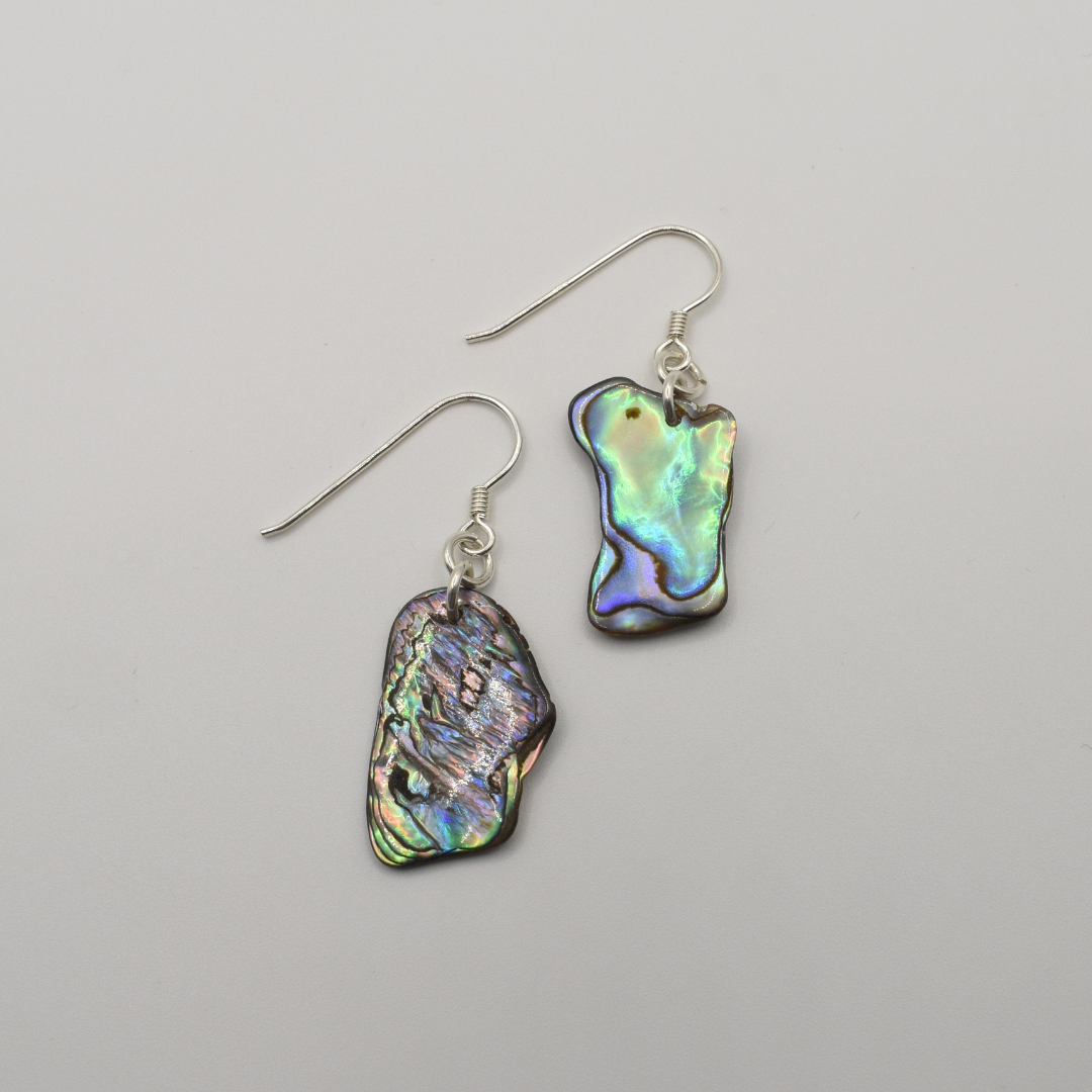 Salty Dreamers’ Earrings | Paua Shell Ruru: Handmade dangly earrings featuring irregular pāua shell pieces in iridescent green, blue, and purple hues, displayed on a plain white background.