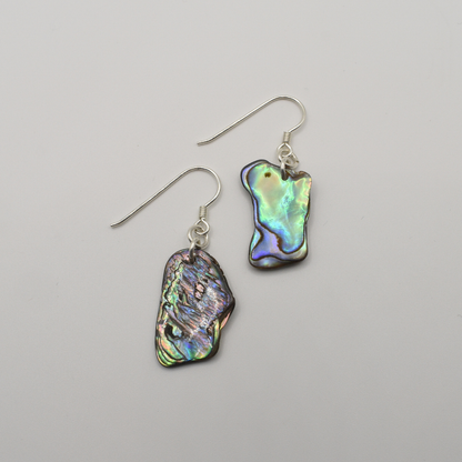 Salty Dreamers’ Earrings | Paua Shell Ruru: Handmade dangly earrings featuring irregular pāua shell pieces in iridescent green, blue, and purple hues, displayed on a plain white background.