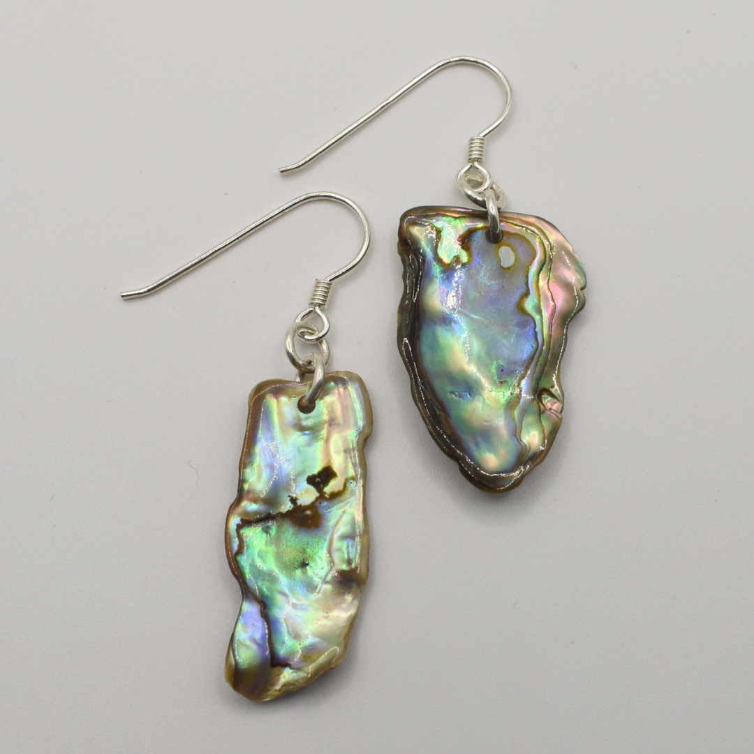 Salty Dreamers Earrings | Paua Shell Kekeno: Handmade silver earrings with irregular, iridescent pāua shell pendants on silver hooks, displayed against a plain light background.