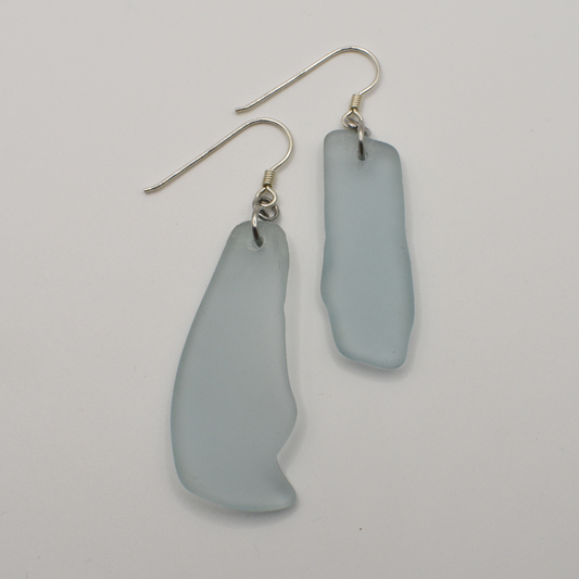 Salty Dreamers Earrings | Seaglass Blue Surfer: Irregularly shaped, frosted light blue sea glass drops on sterling silver hooks, shown on a white background.