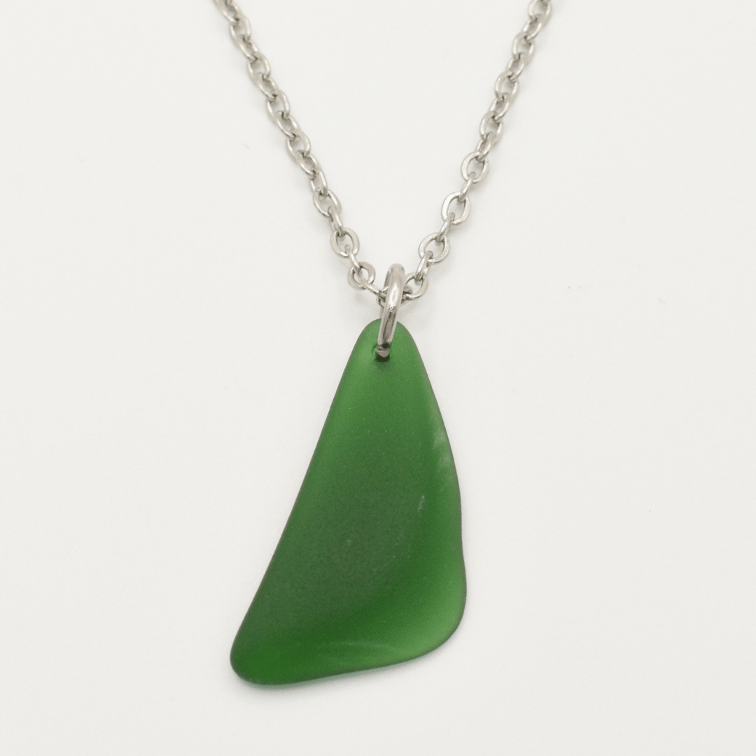 The Salty Dreamers Necklace | Green Sea Glass features a single, irregular green sea glass pendant on a silver chain, crafted in stainless steel and shown against a plain white background.