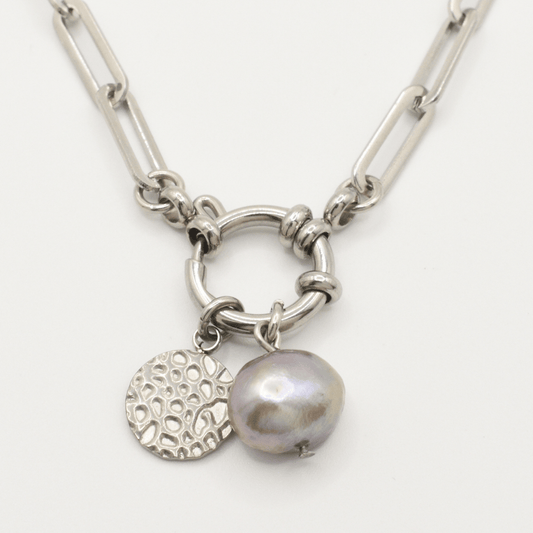 Salty Dreamers' A Cute Couple Pearl Necklace features a silver chain with large links, a circular textured charm, and a metallic lavender irregular freshwater pearl pendant on a hoop-like centerpiece.