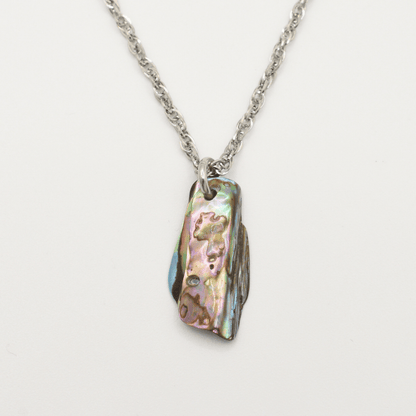 The Salty Dreamers Necklace | Paua Shell Tu features a silver stainless steel chain with a rectangular, iridescent pāua shell pendant in green, pink, and blue on a white background.