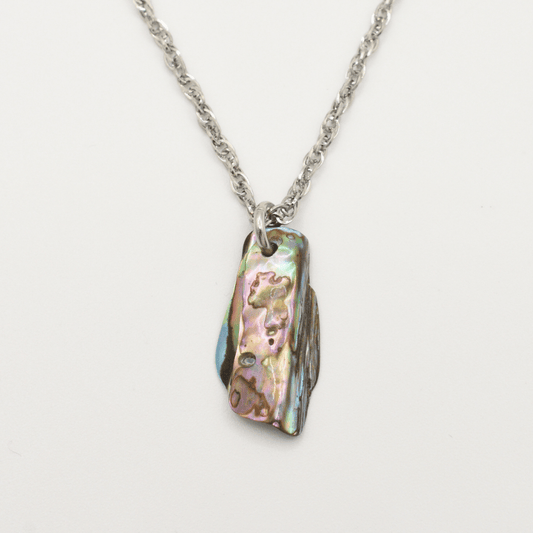 The Salty Dreamers Necklace | Paua Shell Tu features a silver stainless steel chain with a rectangular, iridescent pāua shell pendant in green, pink, and blue on a white background.