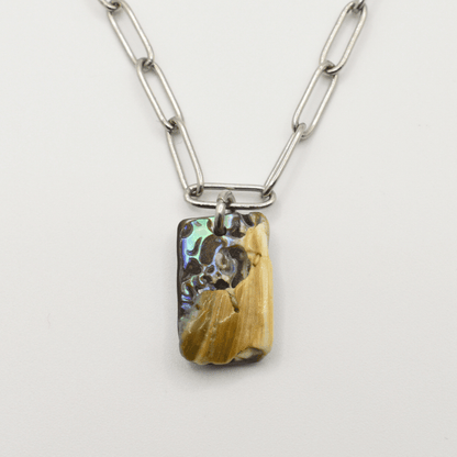 The Salty Dreamers Necklace | Paua Shell Ngaru features a silver chain and rectangular pendant with iridescent pāua shell and tan textured accents—a stunning piece of handmade New Zealand jewelry shown on a white background.