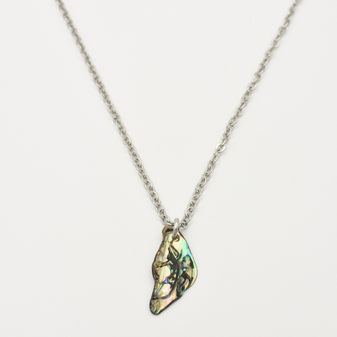 The Salty Dreamers Necklace | Paua Shell Takaro features an irregular, iridescent pāua shell pendant on a silver chain, handmade in New Zealand—an eye-catching piece of jewelry shown on a white background.
