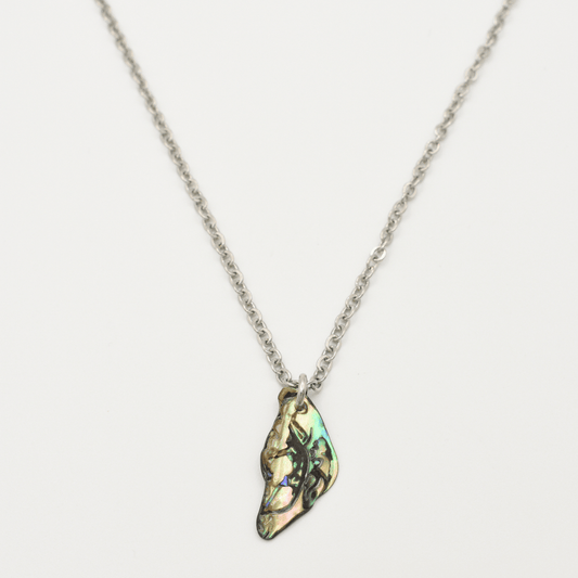 The Salty Dreamers Necklace | Paua Shell Takaro features an irregular, iridescent pāua shell pendant on a silver chain, handmade in New Zealand—an eye-catching piece of jewelry shown on a white background.