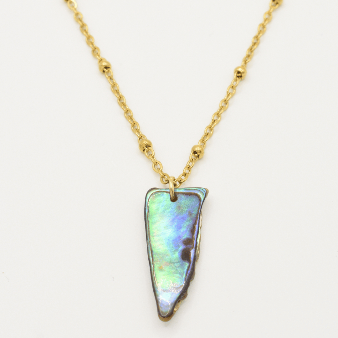 The Paua Shell Hine Necklace by Salty Dreamers features a gold chain with small beads and a triangular New Zealand abalone shell pendant, perfect for handmade jewelry enthusiasts.