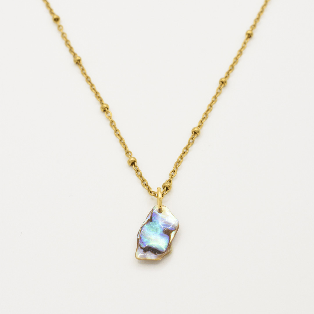 The Salty Dreamers Necklace | Paua Shell Ra features a golden stainless steel beaded chain and an iridescent, irregularly shaped paua shell pendant, shown centered against a plain white background.