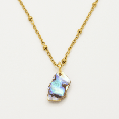 The Salty Dreamers Necklace | Paua Shell Ra features a gold chain with small round beads and an irregular iridescent pāua shell pendant—handmade jewelry shown on a plain white background.