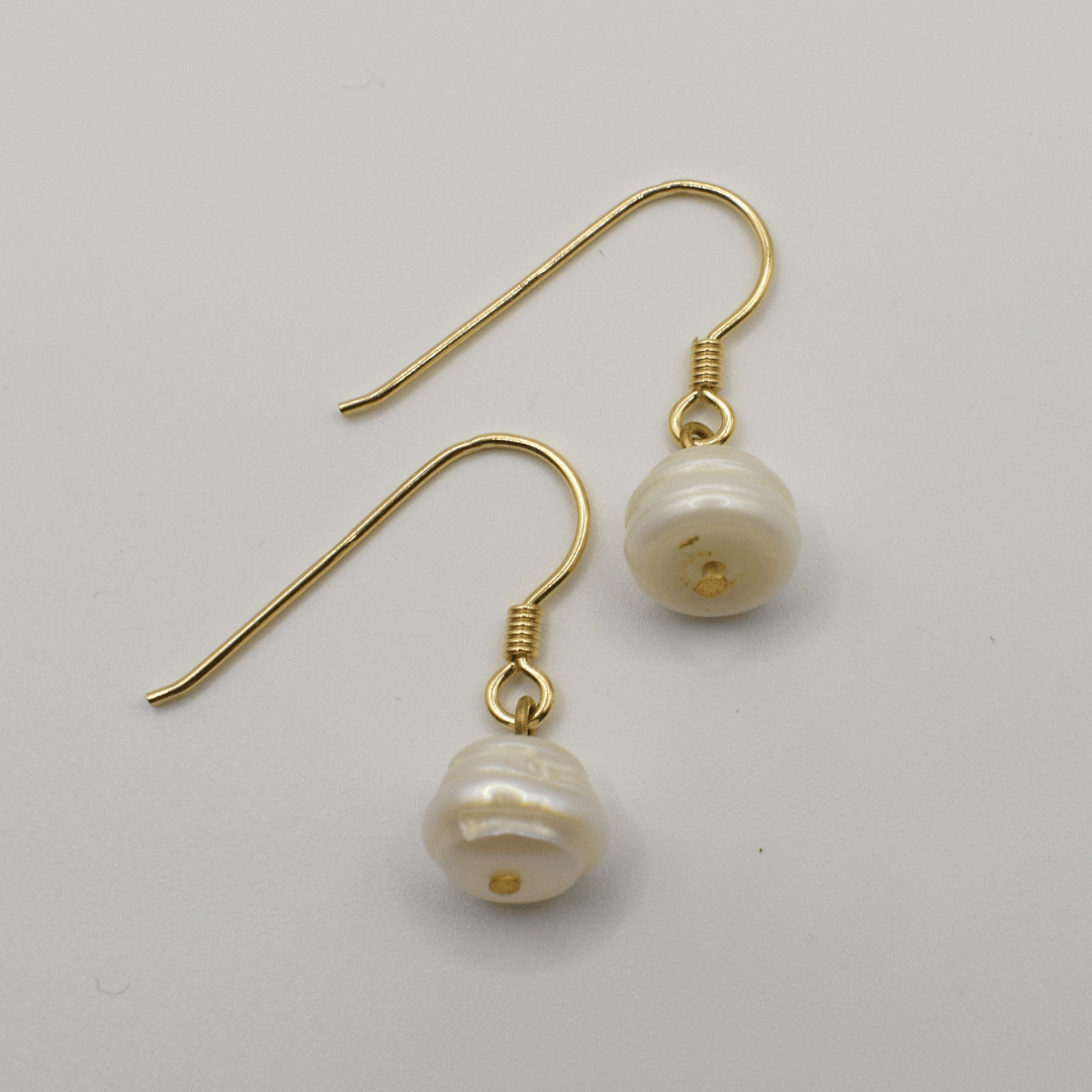 The Pearl earrings by Salty Dreamers feature a single irregular freshwater pearl on each gold earring, shown against a plain white background.