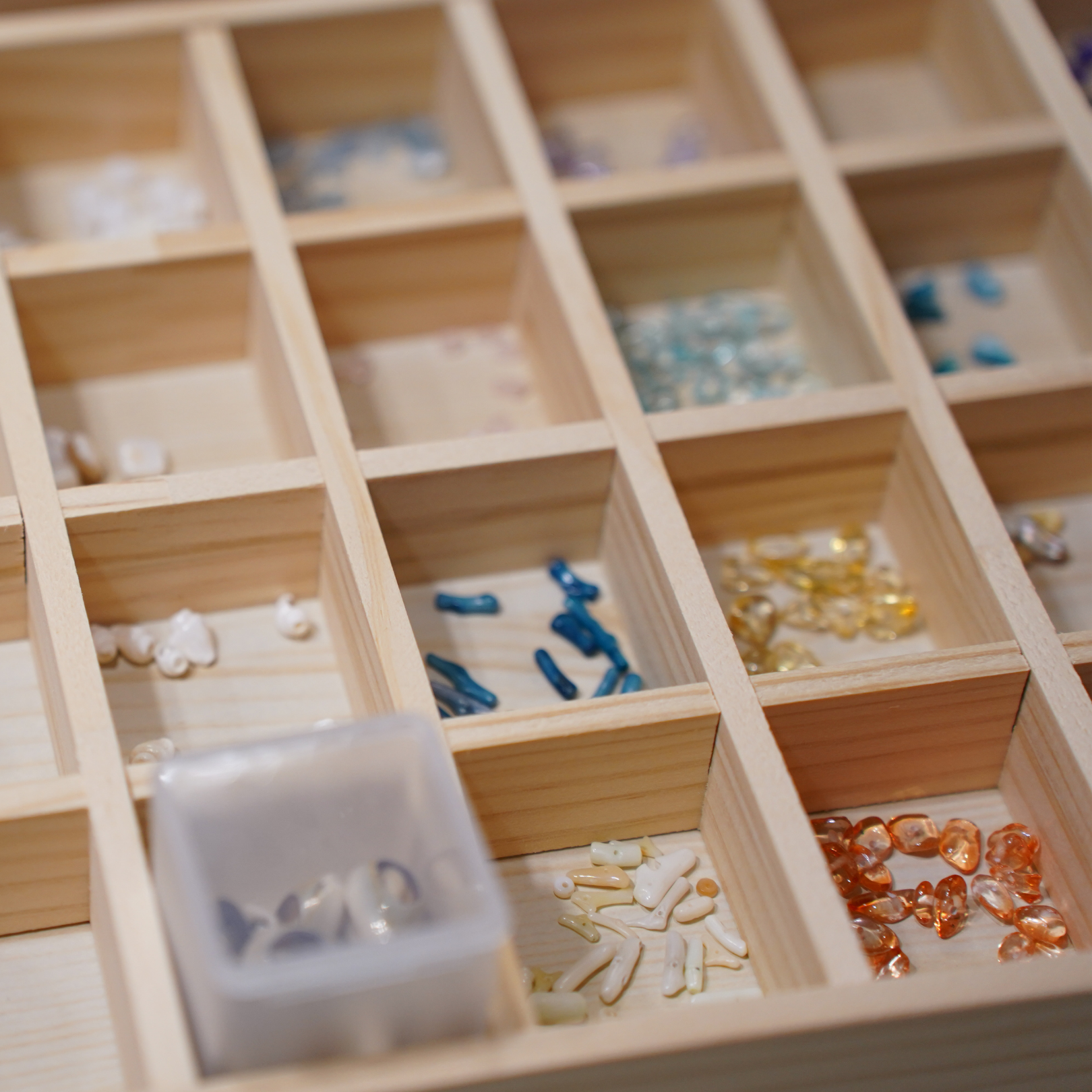 The Salty Dreamers Workshop Ocean Jewellery in Kiel features a wooden organizer with compartments for colorful beads and gemstones, plus a plastic container for extra beads—ideal for creating your own jewelry.