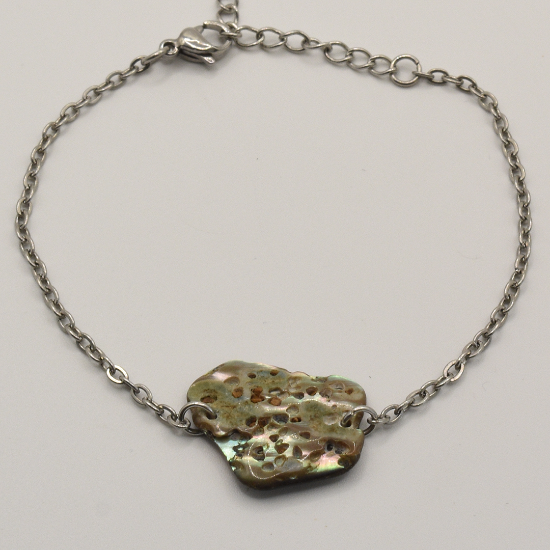 The Paua Shell Hihiri bracelet by Salty Dreamers features a handmade silver chain and an irregular, multicolored centerpiece with earthy tones and a metallic sheen, inspired by ocean jewelry.