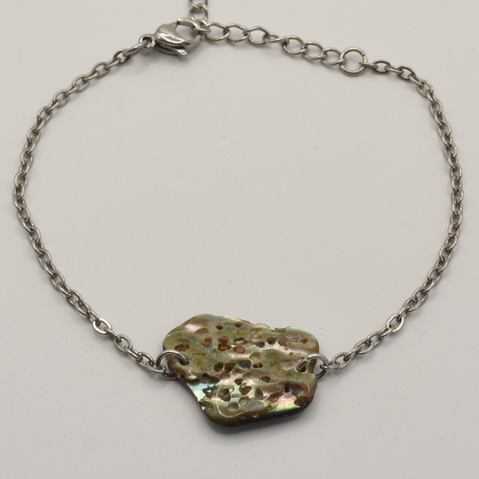 The Paua Shell Hihiri bracelet by Salty Dreamers features a handmade silver chain and an irregular, multicolored centerpiece with earthy tones and a metallic sheen, inspired by ocean jewelry.