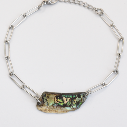 The Salty Dreamers Bracelet | Paua Shell Raumati features a handmade silver chain with elongated links and a central New Zealand paua shell pendant showing iridescent green, gold, and black hues, photographed on a white background.