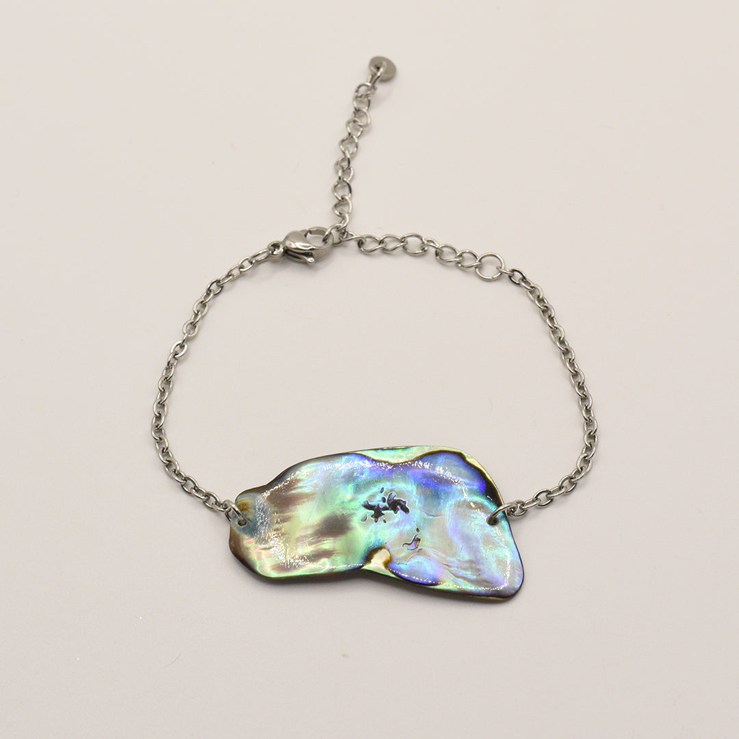 The Salty Dreamers Bracelet | Paua Shell Taurima features a handmade, iridescent pāua shell centerpiece on a silver stainless steel band—an elegant piece of New Zealand jewelry displayed on a white background.