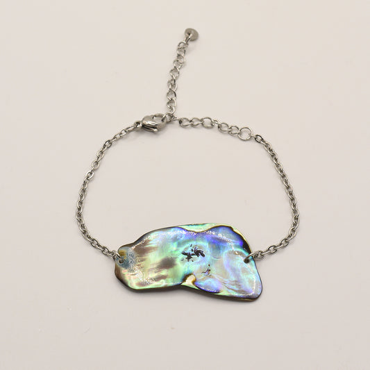 The Salty Dreamers Bracelet | Paua Shell Taurima features a handmade, iridescent pāua shell centerpiece on a silver stainless steel band—an elegant piece of New Zealand jewelry displayed on a white background.