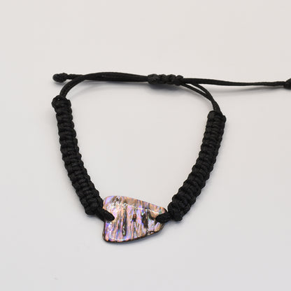 The Salty Dreamers Bracelet | Paua Shell Toa is a handmade black braided cord bracelet featuring an iridescent, irregular New Zealand paua shell centerpiece, shown on a plain white background.
