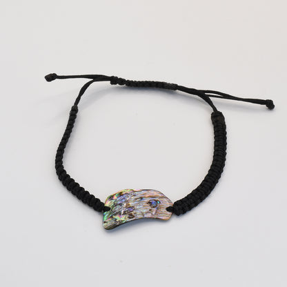 The Salty Dreamers Bracelet | Paua Shell Uru is a handmade black braided bracelet with an iridescent, claw-shaped New Zealand abalone shell centerpiece, shown on a plain white background.