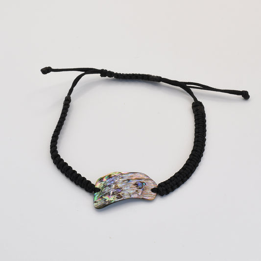 The Salty Dreamers Bracelet | Paua Shell Uru is a handmade black braided bracelet with an iridescent, claw-shaped New Zealand abalone shell centerpiece, shown on a plain white background.