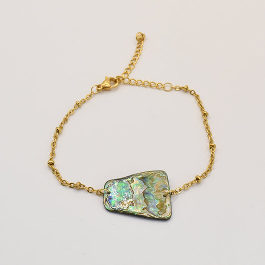 The Bracelet | Paua Shell Whakaora by Salty Dreamers is a handmade gold chain bracelet with an adjustable clasp, featuring a large, irregular pāua shell in iridescent green, blue, and gold on a plain white background.