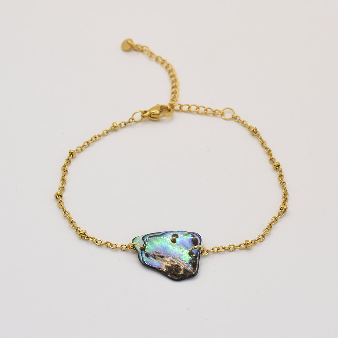 The Salty Dreamers Bracelet | Paua Shell Hau features an eye-catching, irregular iridescent pāua shell centerpiece on a gold chain—an elegant piece of abalone jewelry displayed on a white background.