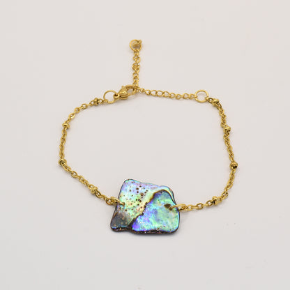The Salty Dreamers Bracelet | Paua Shell Whenua features a delicate gold chain with an iridescent, uniquely shaped pāua shell centerpiece, highlighting abalone jewelry artistry against a plain light background.