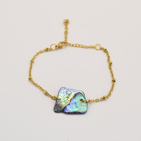 The Salty Dreamers Bracelet | Paua Shell Whenua features a delicate gold chain with an iridescent, uniquely shaped pāua shell centerpiece, highlighting abalone jewelry artistry against a plain light background.