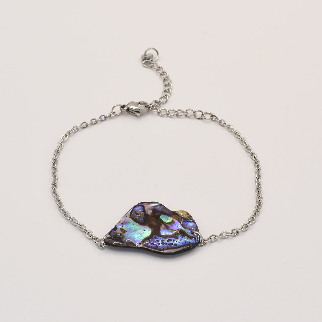 The Salty Dreamers Bracelet | Paua Shell Ngaru features a silver chain and an irregular New Zealand pāua shell centerpiece with vibrant blue, green, and purple tones, showcased on a plain white background.