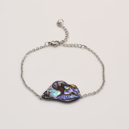 The Salty Dreamers Bracelet | Paua Shell Ngaru features a silver chain and an irregular New Zealand pāua shell centerpiece with vibrant blue, green, and purple tones, showcased on a plain white background.