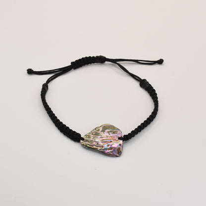 The Salty Dreamers Bracelet | Paua Shell Kaha features an irregular, iridescent pāua shell on a black braided cord, reflecting the beauty of New Zealand jewelry against a plain white background.