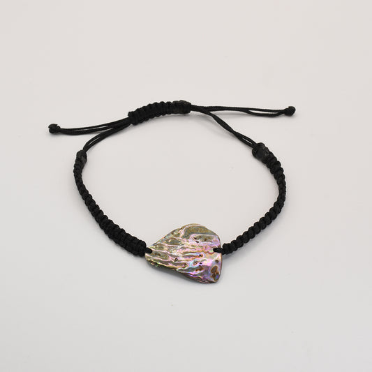 The Salty Dreamers Bracelet | Paua Shell Kaha features an irregular, iridescent pāua shell on a black braided cord, reflecting the beauty of New Zealand jewelry against a plain white background.