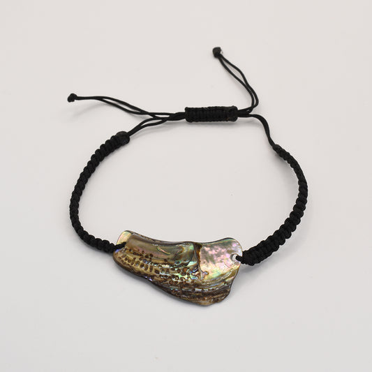 The Salty Dreamers Bracelet | Paua Shell Ngakau is a black braided handmade piece with an iridescent, irregular New Zealand abalone shell centerpiece, shown on a plain white background.