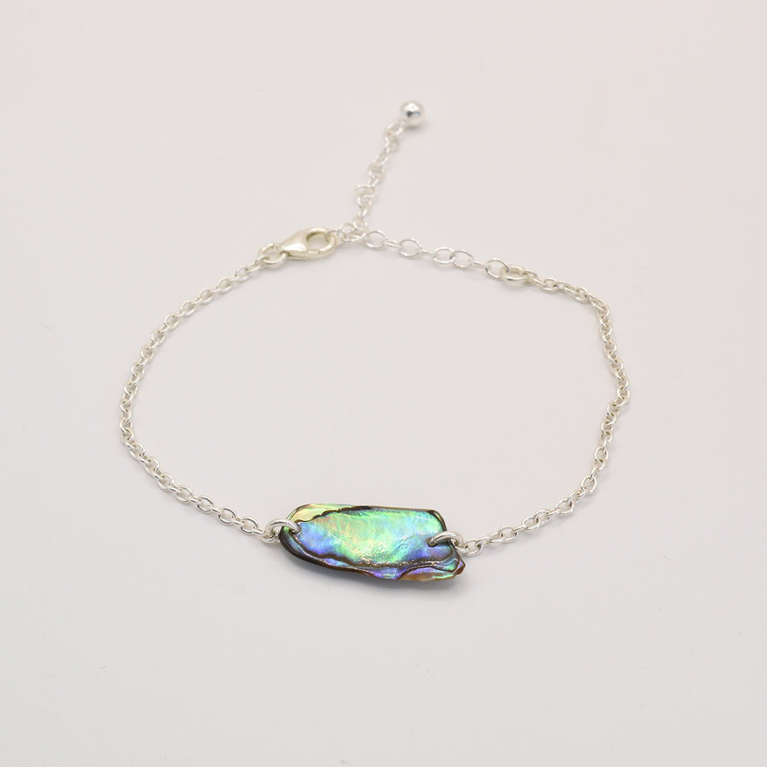 The Salty Dreamers Bracelet | Paua Shell Toi is a handmade silver chain bracelet showcasing an iridescent, irregular New Zealand pāua shell centerpiece, displayed on a plain white background.