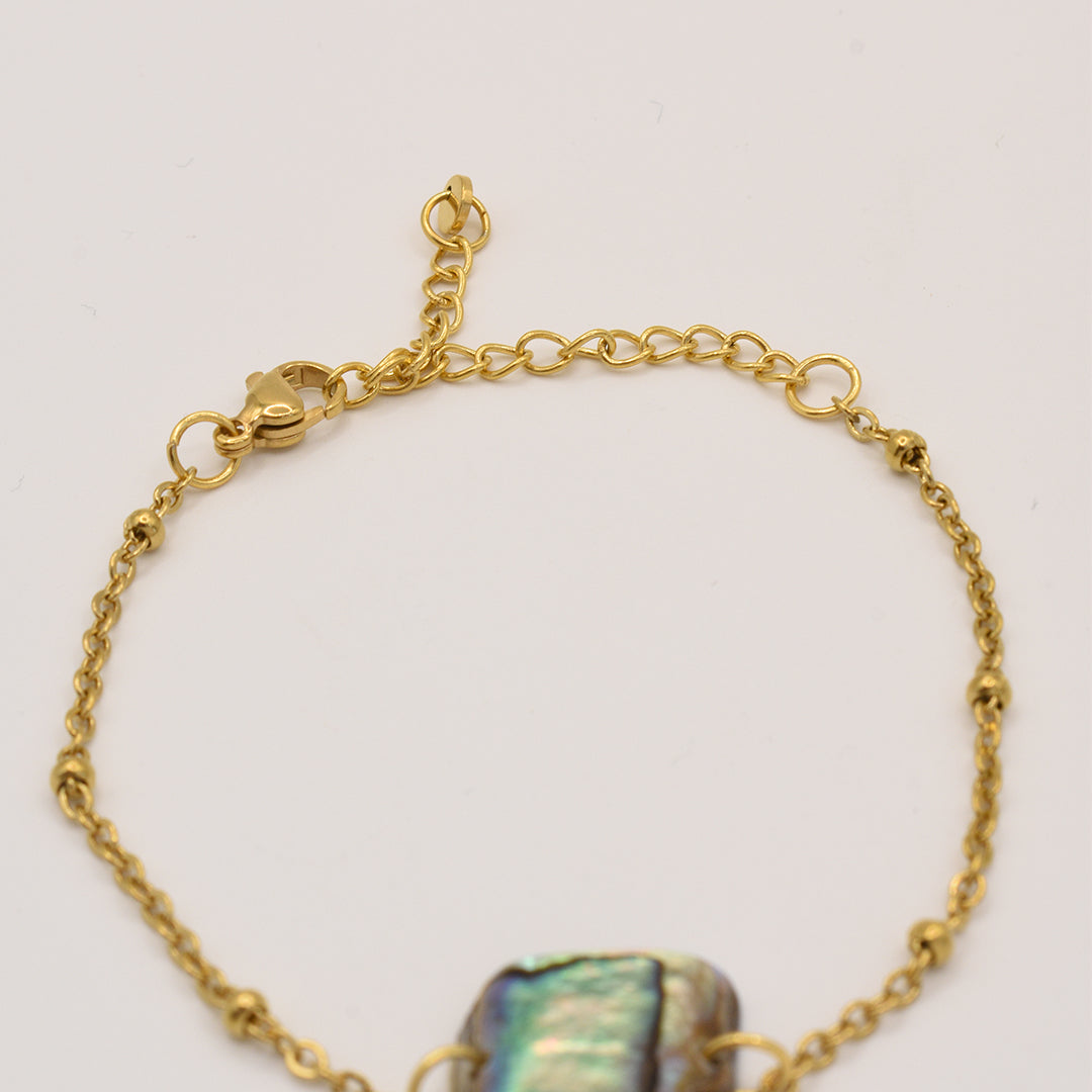 The Salty Dreamers Bracelet | Paua Shell Pae features a gold chain with a lobster clasp, extender, and central iridescent pāua shell bead—ideal for fans of handmade New Zealand jewelry. Displayed on a simple light background.