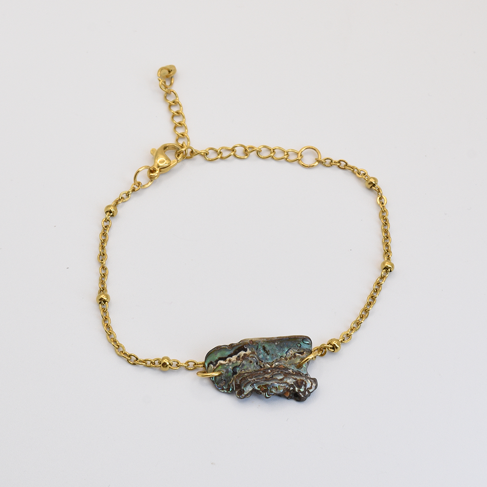 The Salty Dreamers Bracelet | Paua Shell Marie features a delicate gold chain and an irregularly shaped pāua shell with blue-green hues at the center, shown on a plain white background.