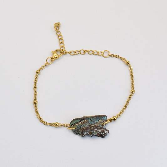 The Salty Dreamers Bracelet | Paua Shell Marie features a delicate gold chain and an irregularly shaped pāua shell with blue-green hues at the center, shown on a plain white background.