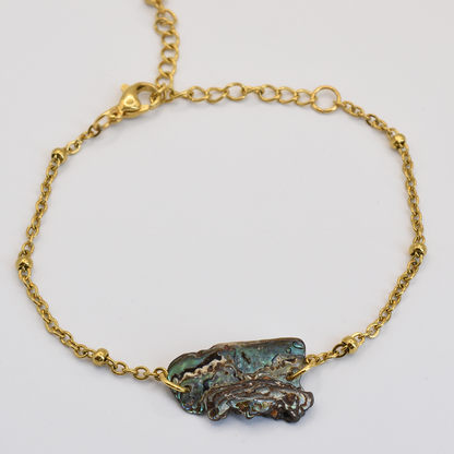 The Bracelet | Paua Shell Marie by Salty Dreamers features a delicate gold chain and an irregular, textured pāua shell centerpiece in blue-green tones—a striking piece of New Zealand jewelry, shown on a plain white background.