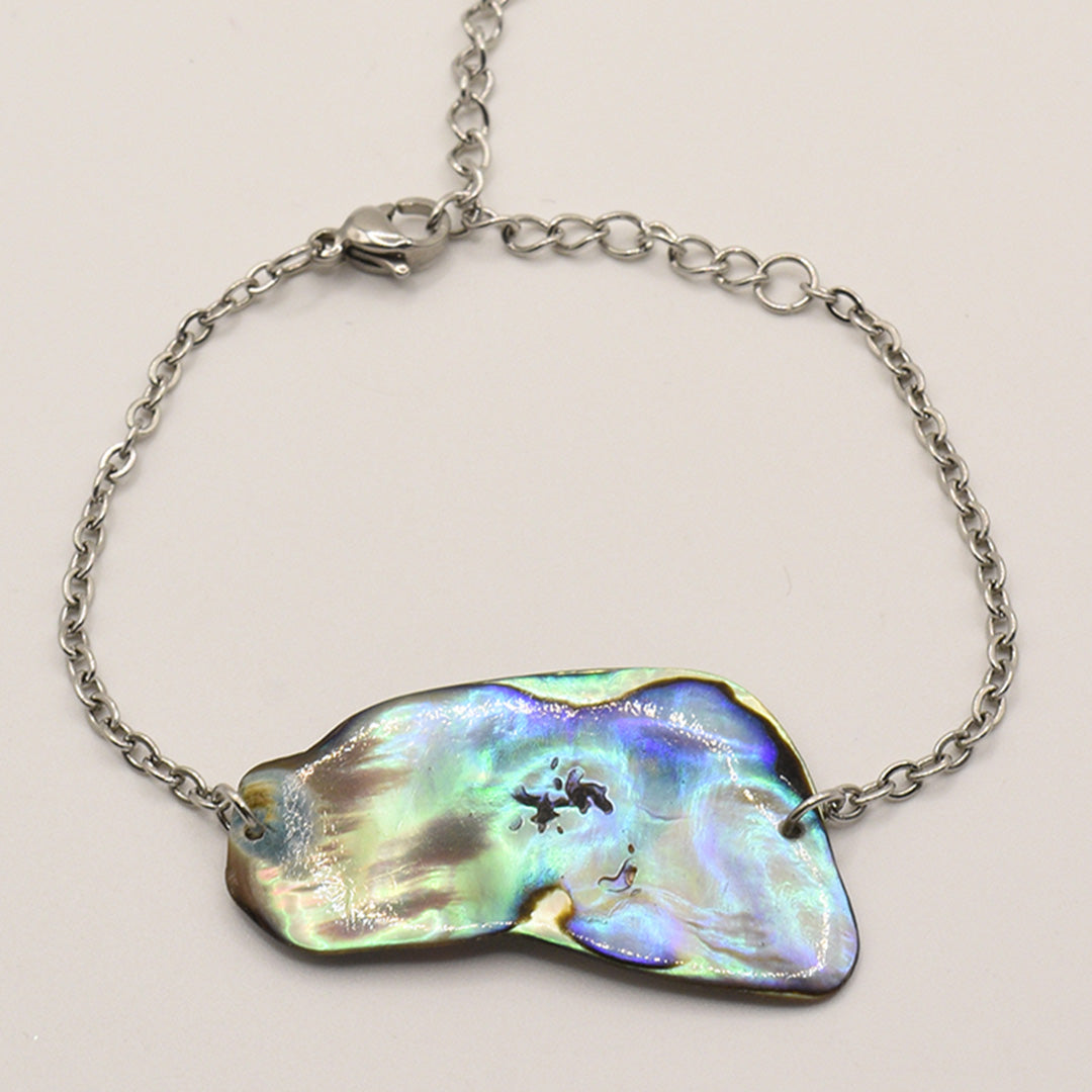 The Salty Dreamers Bracelet | Paua Shell Taurima features a handmade silver chain with an iridescent, irregular pāua shell centerpiece and a lobster clasp, displayed on a plain background.