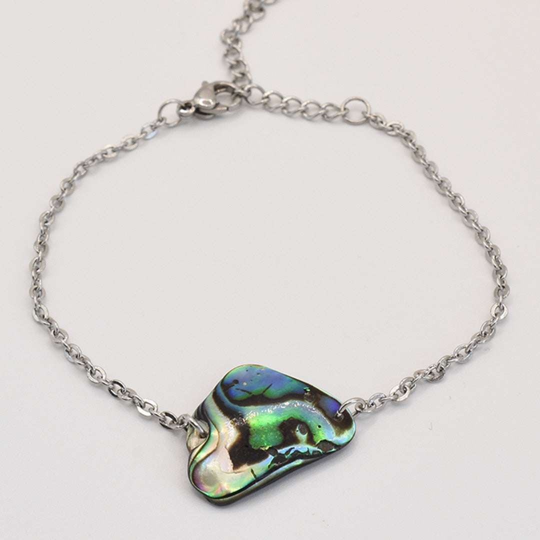The Bracelet | Paua Shell Tai by Salty Dreamers features an iridescent, irregular New Zealand abalone centerpiece in green, blue, and black—a handmade silver chain bracelet inspired by the ocean.
