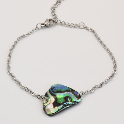 The Bracelet | Paua Shell Tai by Salty Dreamers features an iridescent, irregular New Zealand abalone centerpiece in green, blue, and black—a handmade silver chain bracelet inspired by the ocean.