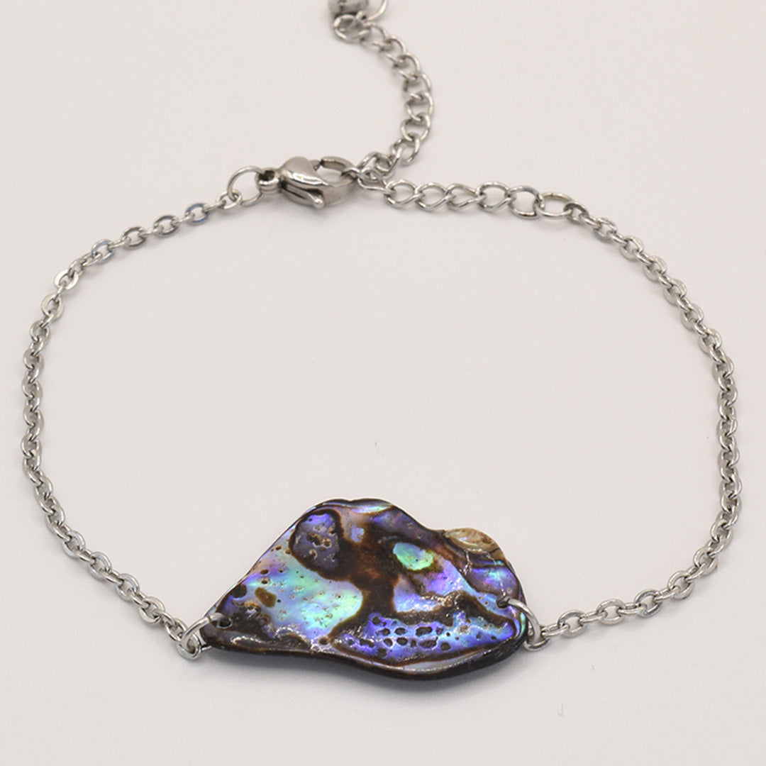 The Salty Dreamers Bracelet | Paua Shell Ngaru features a silver chain and an irregularly shaped, iridescent blue and purple pāua shell centerpiece with natural patterns, shown on a white background.