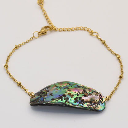 The Paua Shell Mahaki bracelet by Salty Dreamers features an iridescent pāua shell centerpiece in green, blue, and purple on a gold chain with a lobster clasp—a striking piece of handmade New Zealand jewelry.