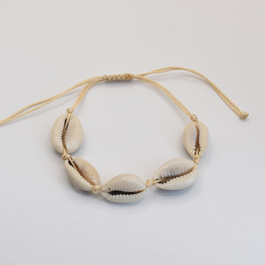 The Salty Dreamers Bracelet | Cowrie Away Beige features five white cowrie shells on a light tan adjustable macramé cord, beautifully displayed against a plain white background.