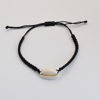 The Salty Dreamers Macramazing Cowrie Black bracelet features a handmade black braided band with a single white cowrie shell at the center, shown on a plain white background.