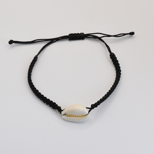 The Salty Dreamers Macramazing Cowrie Black bracelet features a handmade black braided band with a single white cowrie shell at the center, shown on a plain white background.