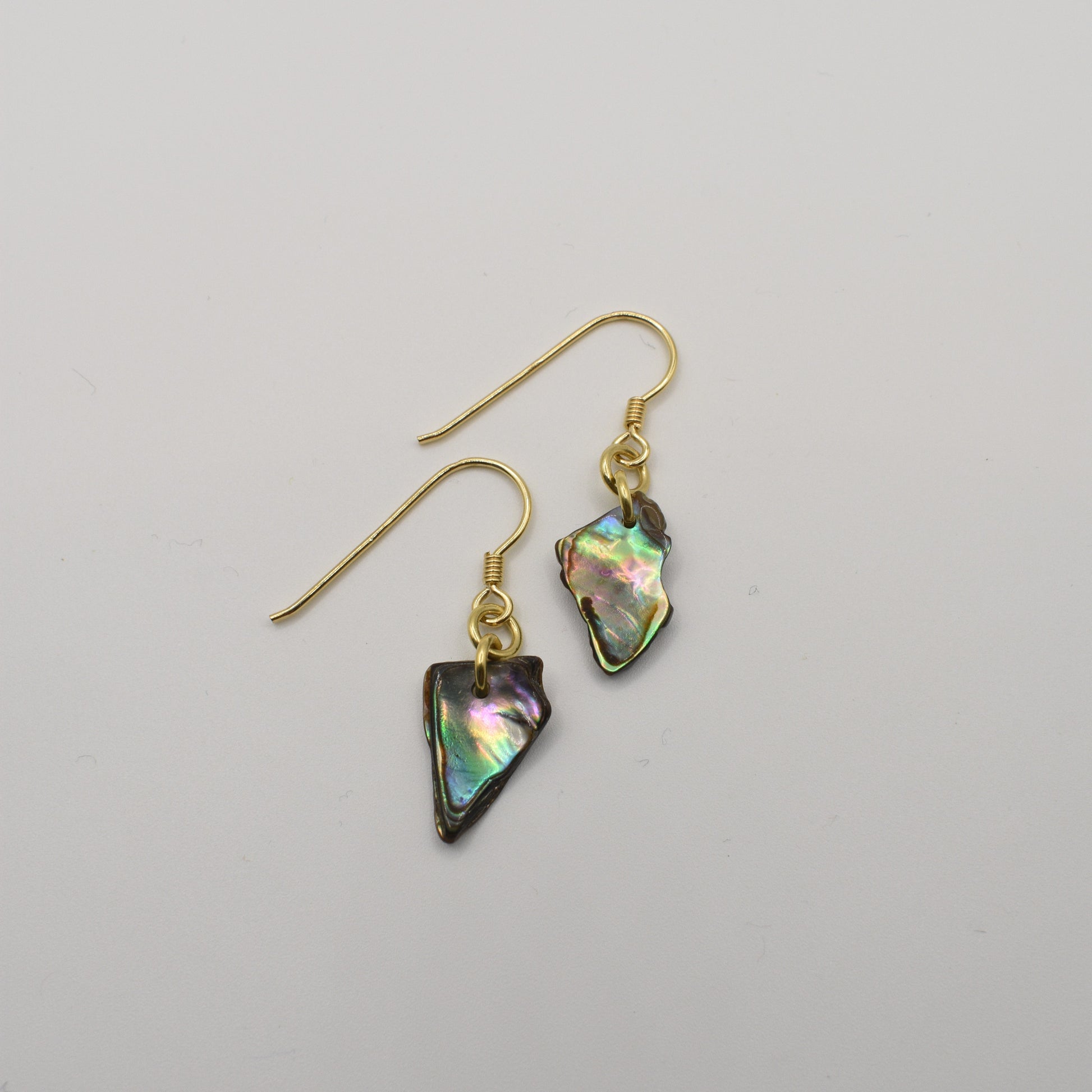 The Salty Dreamers Earrings | Paua Shell Uru feature gold-plated silver hooks and unique, iridescent pāua shell pendants, showcasing New Zealand artistry, set against a plain white background.