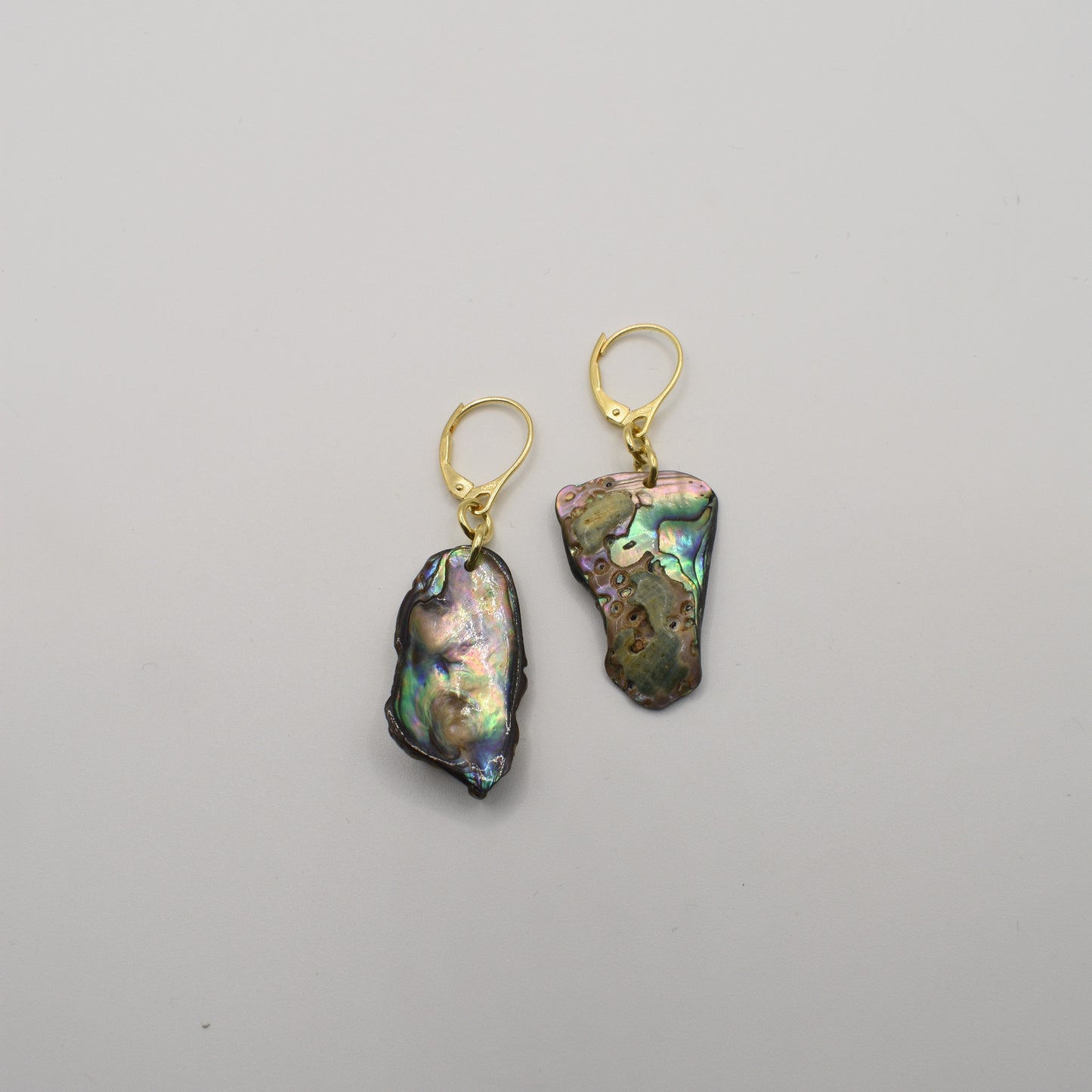 The Salty Dreamers Earrings | Paua Shell Marie feature two asymmetrical iridescent paua shell pieces with gold-plated silver lever-back hooks, shown on a plain white background.