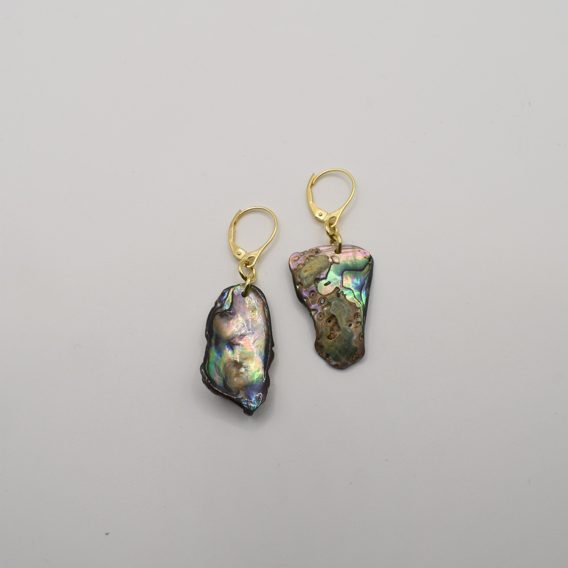 The Salty Dreamers Earrings | Paua Shell Marie feature two asymmetrical iridescent paua shell pieces with gold-plated silver lever-back hooks, shown on a plain white background.