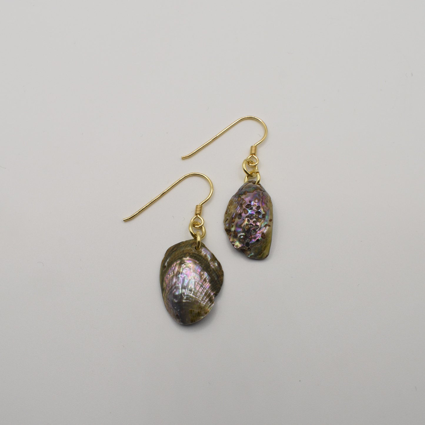 The Salty Dreamers Earrings | Paua Shell Mahaki feature irregular, iridescent pāua shell pendants on gold-plated silver hooks, shown against a plain white background.
